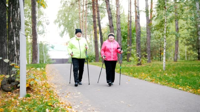 Two-elderly-women-are-doing-Scandinavian-walking-in-the-park.-Mid-shot