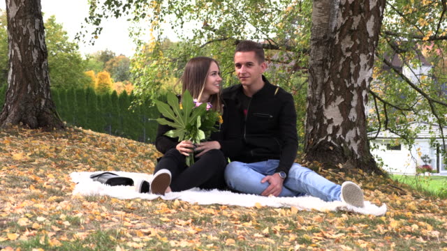 A-young-couple-sits-on-a-white-bedspread-in-autumn-park