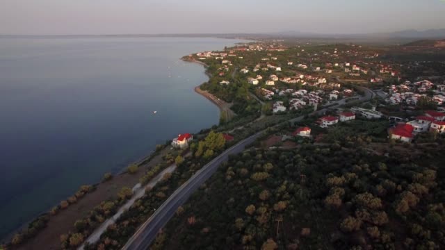 Flying-over-Trikorfo-Beach-coastline-with-cottages-and-green-uplands,-Greece