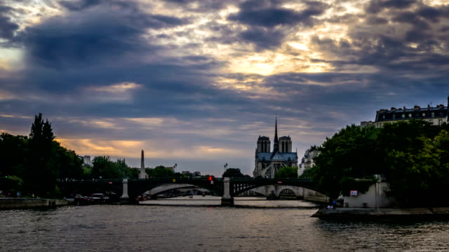 Timelapse-beleuchtete-Boote-in-Paris-bei-Nacht,-mit-Notre-Dame-De-Paris-Kathedrale-im-Hintergrund-Blick-von-Henri-II-Brücke