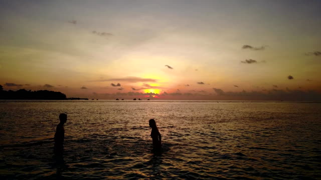 v04134-vuelo-drone-vista-aérea-de-Maldivas-playa-2-personas-pareja-hombre-mujer-amor-romántico-puesta-de-sol-salida-del-sol-en-la-isla-de-paraíso-tropical-soleado-con-cielo-azul-aqua-agua-mar-4k