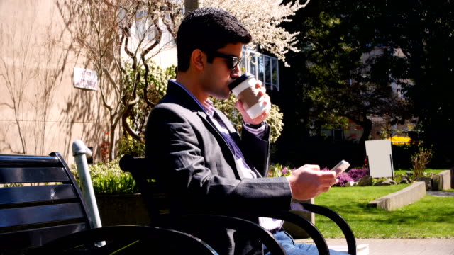 Hombre-usando-teléfono-móvil-tomando-café-en-el-Parque-4k