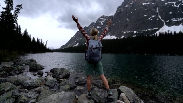 Hiker-female-arms-outstretched-by-mountain-lake