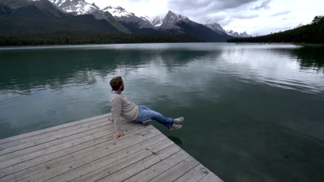 Hombre-joven-en-el-muelle-del-lago-mirando-el-paisaje-de-montaña-en-Canadá