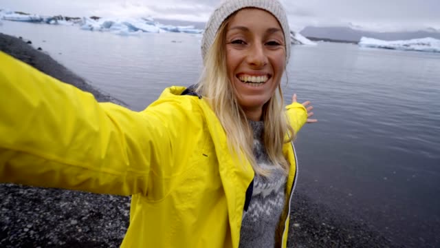 4K-Young-woman-taking-selfie-with-glacier-lake,-icebergs-floating-on-water