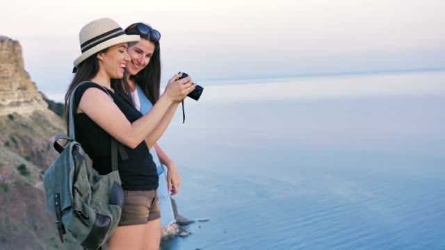 Zwei-attraktive-weibliche-Reisende-nehmen-Foto-schöne-Meer-Landschaft-mit-professioneller-Kamera