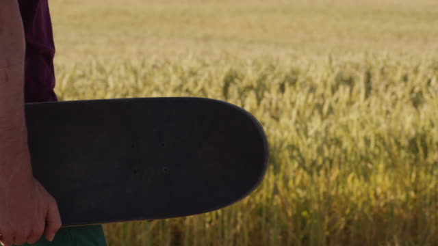 Adult-walking-next-to-Beautiful-wheat-field-holding-skateboard-with-blue-sky-and-epic-sun-light---shot-on-RED