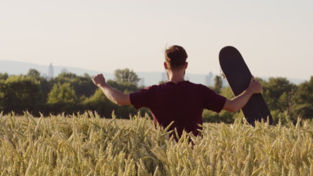 Erwachsene-stehen-bei-der-Beschaffung-von-Beautiful-Weizen-Feld-skateboard-mit-Stadt-im-Hintergrund---Schuss-auf-rot