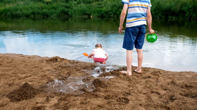 Juego-de-los-niños-en-el-río-en-el-verano,-la-niña-recoge-agua-del-río-y-se-vierte-en-la-arena
