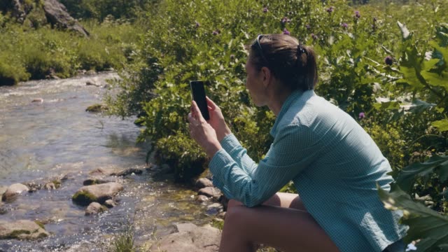 Mujer-turista-descansando-en-la-orilla-del-río-y-haciendo-fotos-con-el-teléfono-móvil