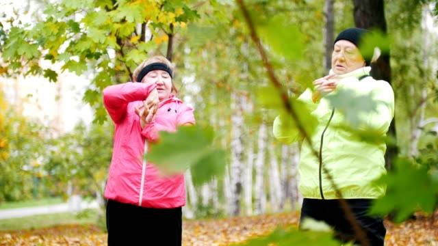 Mujer-madura-en-chaquetas-coloridas-haciendo-gimnasia-en-un-parque-de-otoño-después-de-una-caminata-escandinava