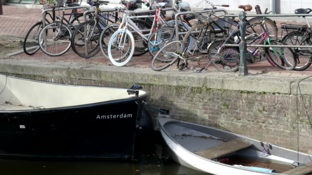 zahlreiche-Fahrräder-und-der-Bug-eines-Bootes-an-einem-Kanal-in-amsterdam