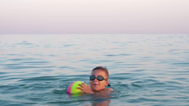 Glückliches-Kind-Baden-im-Meer-mit-ball
