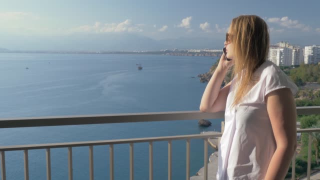 Frau-mit-Telefon-reden-und-genießen-Sie-Meerblick-vom-Balkon