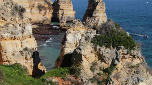 Ponta-da-Piedade,-lugar-famoso-en-el-sur-de-Portugal,-la-ciudad-de-lagos,-la-costa-rocosa,-olas-de-océano-Atlántico,-rocas-afiladas,-agua-azul,-flores-amarillas,-arco,-nadie,-playa-salvaje