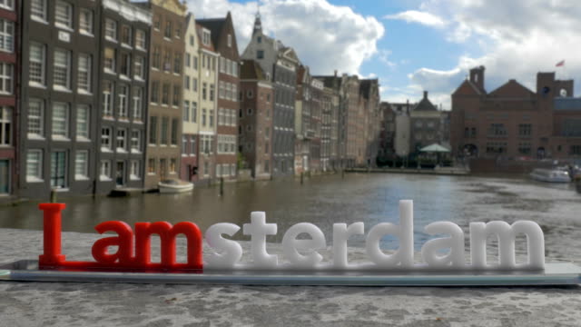 Vista-de-figurita-plástico-de-la-escultura-de-Iamsterdam-letras-sobre-el-puente-contra-el-paisaje-borroso,-Ámsterdam,-Países-Bajos