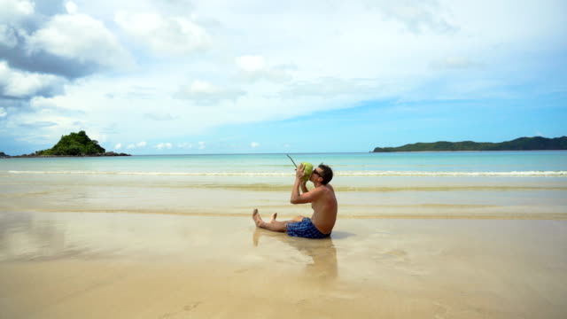 Man-drinks-coconut-juice-from-a-nut-on-a-beach-at-the-ocean