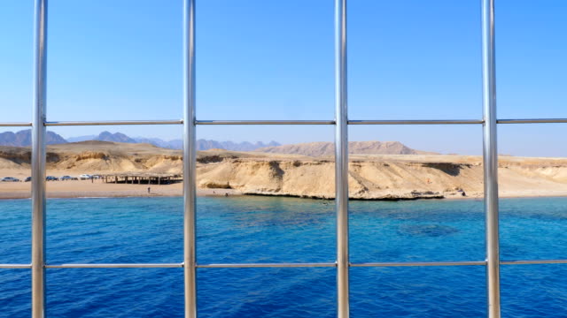 summer,-sea,-through-a-metal-fence-on-the-deck-you-can-see-a-beautiful-seascape.-deserted-shore,-tents-and-machines-of-Bedouins