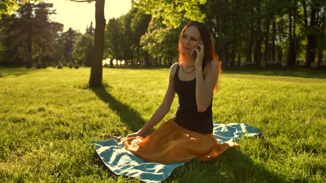 Female-sitting,-talking-during-a-phone-call-outdoors-in-the-park