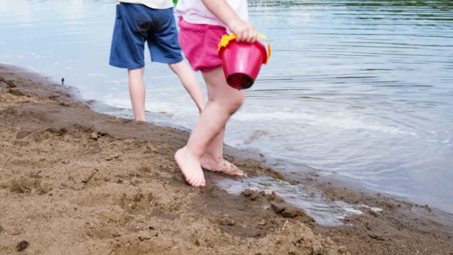Niña-y-niño-sacar-agua-del-río-con-un-cubo,-movimiento-lento.-Los-niños-juegan-en-la-naturaleza-en-la-arena-de-la-playa