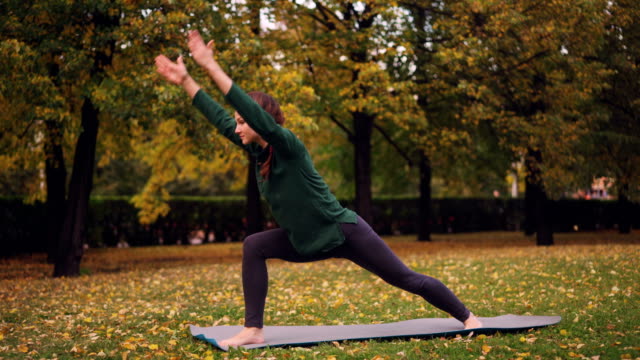 Slender-young-lady-is-doing-yoga-outdoors-changing-asanas-and-enjoying-movement,-fresh-air-and-autumn-nature.-Millennials,-healthy-lifestyle-and-recreation-concept.