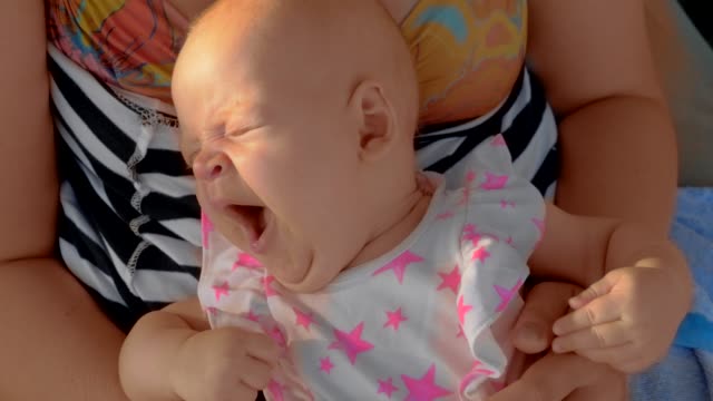 Sleepy-baby-yawning-when-lying-on-mothers-lap-outdoor