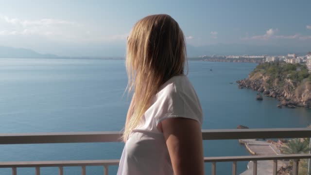 Una-mujer-rubia-hablando-con-un-teléfono-en-un-balcón-del-hotel-cerca-del-paisaje-de-mar
