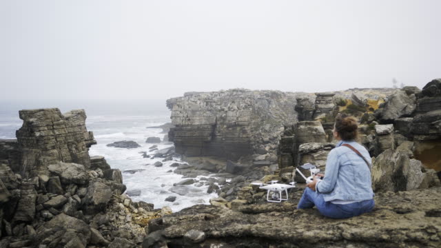 Anonymous-woman-with-drone-sitting-on-seashore