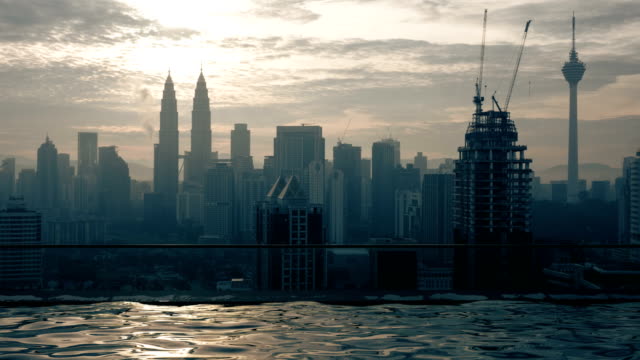 Time-lapse-view-of-swimming-pool-on-the-skyscraper-roof-against-sunrise-building-cityscape.-Kuala-Lumpur,-Malaysia
