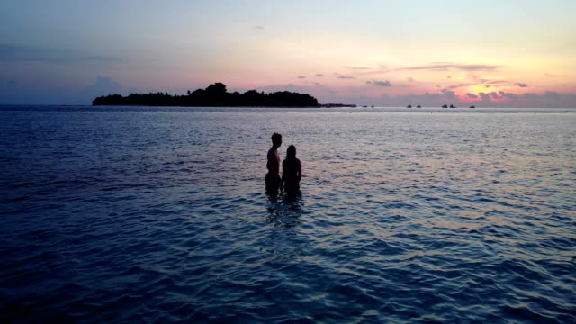 v04157-vuelo-drone-vista-aérea-de-Maldivas-playa-2-personas-pareja-hombre-mujer-amor-romántico-puesta-de-sol-salida-del-sol-en-la-isla-de-paraíso-tropical-soleado-con-cielo-azul-aqua-agua-mar-4k