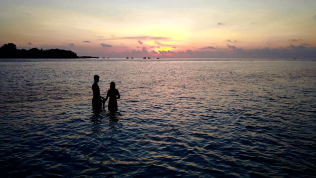 v04149-vuelo-drone-vista-aérea-de-Maldivas-playa-2-personas-pareja-hombre-mujer-amor-romántico-puesta-de-sol-salida-del-sol-en-la-isla-de-paraíso-tropical-soleado-con-cielo-azul-aqua-agua-mar-4k