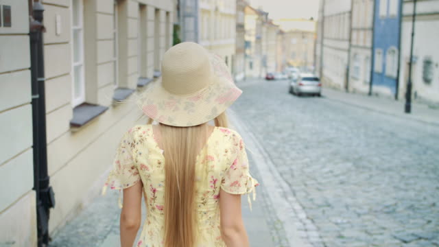 Sonriente-mujer-caminando-en-la-calle.-Mujer-bonita-alegre-en-sombrero-blanco-mirando-hacia-atrás-en-cámara-mientras-camina-en-la-ciudad