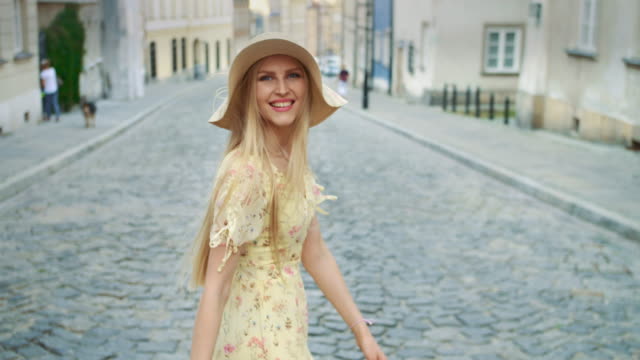 Smiling-woman-walking-on-street.-Cheerful-pretty-woman-in-white-hat-looking-back-at-camera-while-walking-in-town