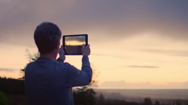 Hombre-de-fotografiar-la-puesta-de-sol-a-través-de-la-tableta-Digital-4K