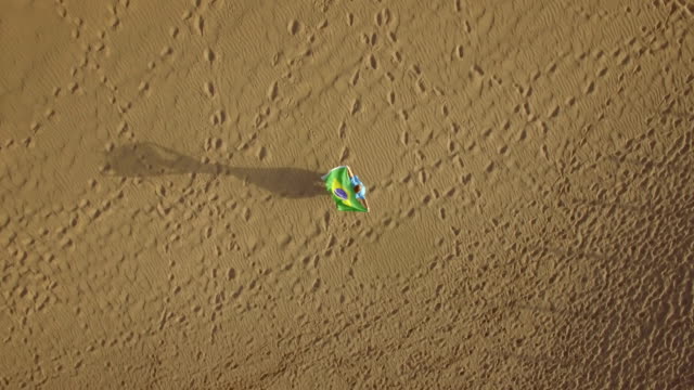 Woman-on-the-sand-with-Brazilian-flag,-aerial-shot