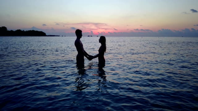 v04169-vuelo-drone-vista-aérea-de-Maldivas-playa-2-personas-pareja-hombre-mujer-amor-romántico-puesta-de-sol-salida-del-sol-en-la-isla-de-paraíso-tropical-soleado-con-cielo-azul-aqua-agua-mar-4k