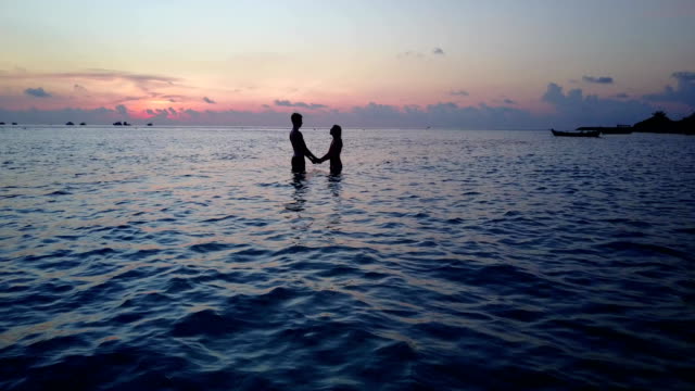 v04165-vuelo-drone-vista-aérea-de-Maldivas-playa-2-personas-pareja-hombre-mujer-amor-romántico-puesta-de-sol-salida-del-sol-en-la-isla-de-paraíso-tropical-soleado-con-cielo-azul-aqua-agua-mar-4k
