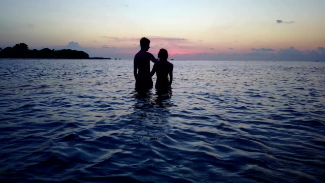 v04177-vuelo-drone-vista-aérea-de-Maldivas-playa-2-personas-pareja-hombre-mujer-amor-romántico-puesta-de-sol-salida-del-sol-en-la-isla-de-paraíso-tropical-soleado-con-cielo-azul-aqua-agua-mar-4k