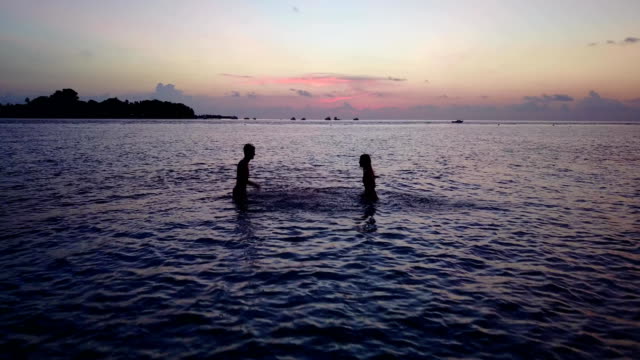 v04183-vuelo-drone-vista-aérea-de-Maldivas-playa-2-personas-pareja-hombre-mujer-amor-romántico-puesta-de-sol-salida-del-sol-en-la-isla-de-paraíso-tropical-soleado-con-cielo-azul-aqua-agua-mar-4k