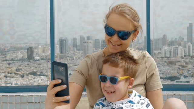 Mother-and-kid-on-hotel-rooftop-taking-selfie-with-cell.-Tel-Aviv,-Israel