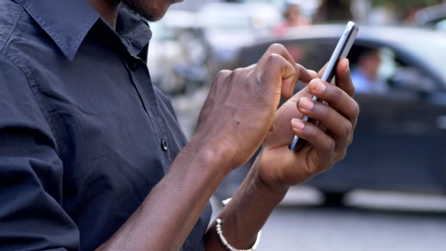 comunicaciones,-dispositivos,-juventud.-Negro-de-manos-de-hombre-escribiendo-en-smartphone-al-aire-libre