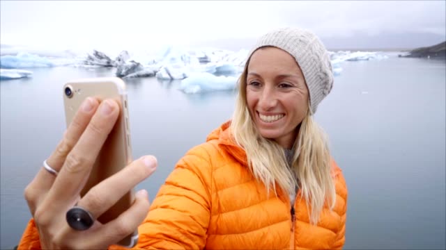 Retrato-de-selfie-de-vídeo-lenta-de-mujer-joven-de-pie-junto-a-la-laguna-glaciar-en-Islandia