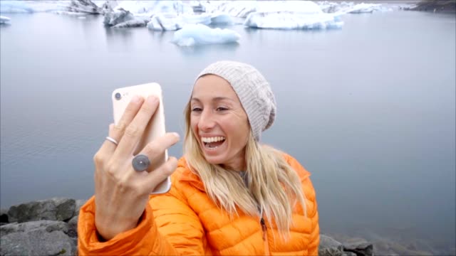 Retrato-de-selfie-de-vídeo-lenta-de-mujer-joven-de-pie-junto-a-la-laguna-glaciar-en-Islandia