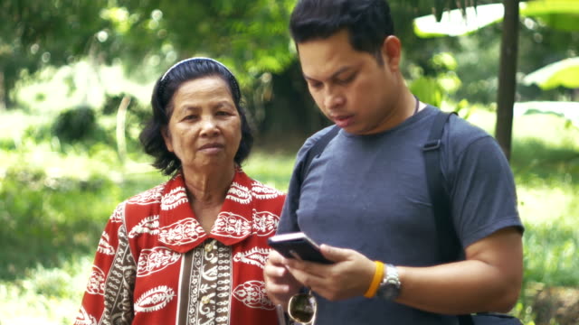 Asian-mother-and-son-rest-in-garden-while-son-using-smartphone-in-morning.
