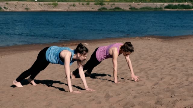 Dos-mujeres-haciendo-deportes-ejercicios-a-orillas-del-río-en-la-ciudad.-Ejercicios-para-las-manos-en-la-tabla.