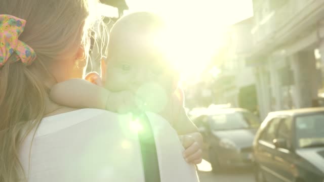 Mum-with-baby-walking-outside-against-bright-sun-flare