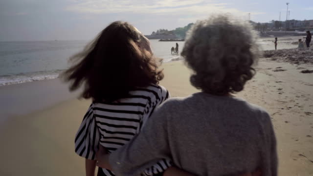 Zwei-lächelnde-Frauen-umarmten-und-Wandern-am-tropischen-Strand.