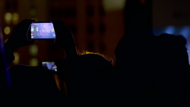 Spectator-man-recording-video-with-zoom-of-stage-and-big-screen-via-smartphone-at-outdoor-music-concert