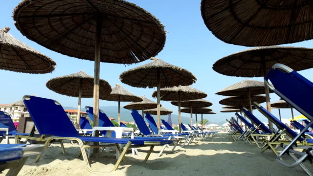 Spaziergang-am-Sandstrand-unter-Sonnenschirmen-und-Liegestühlen.-Urlaub-am-Meer,-schöner-Strand-und-Stroh-Schirme-unter-blauem-Himmel,-4-k-Steadicam-Schuss