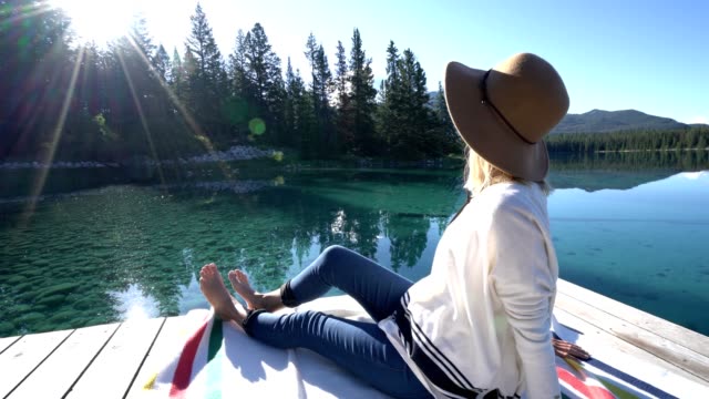 Mujer-sentada-en-el-muelle-de-madera-por-el-impresionante-lago-alpino-contemplando-la-naturaleza